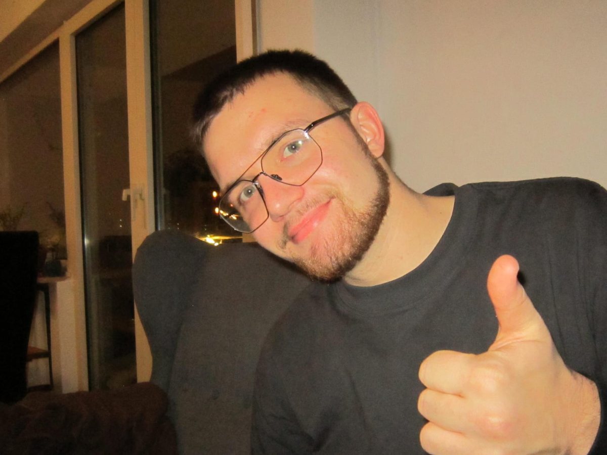 Fabian mit Brille und Bart, lächelt und zeigt Daumen hoch